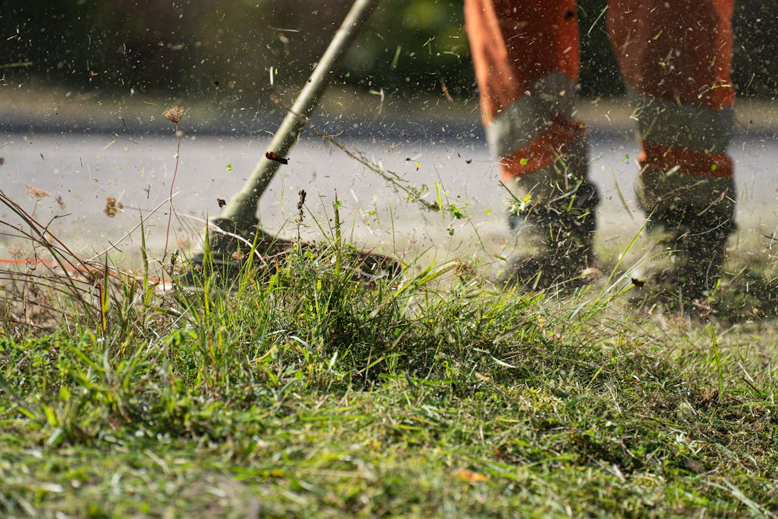 Landscape maintenance worker using a string trimmer to manage grass and overgrowth, helping create clean transitions between planting areas, turf, and hardscape features
