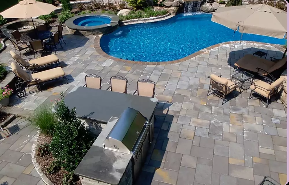 Outdoor living area with kitchen, pool, and seating space in a landscaped backyard